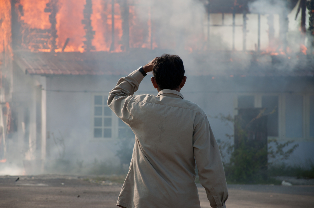 A man holds his head in stress while watching a fire burn his home.